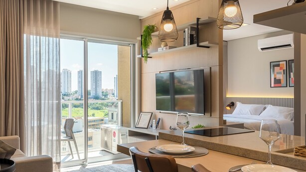 A modern kitchen with a large island, bar stools, a flat-screen TV, and a dining area with a view of the city. - Charming Studio in Cambuí (Campinas)