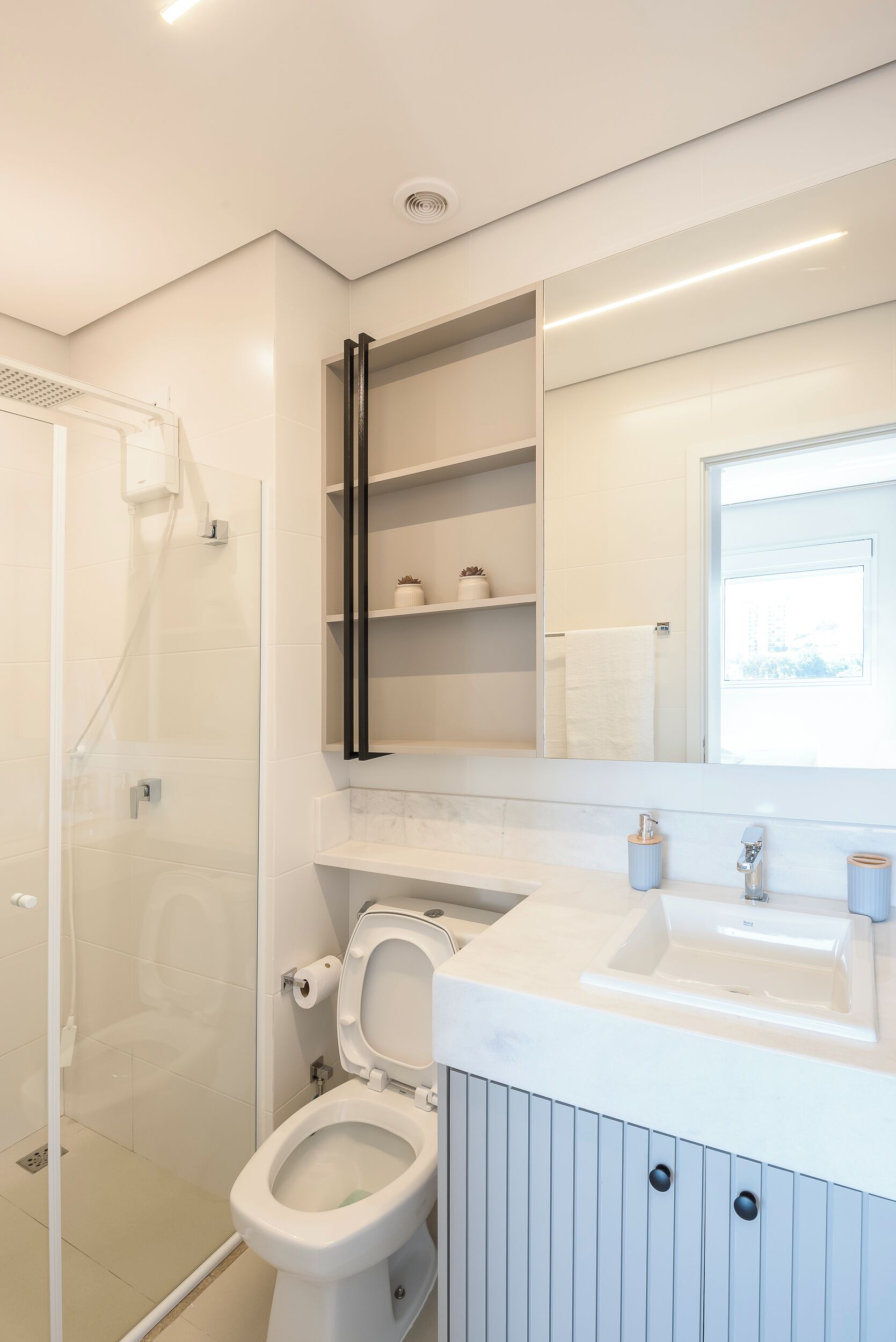 Een moderne badkamer met een douchecabine van glas, een wit toilet en een wastafel met spiegel en planken.