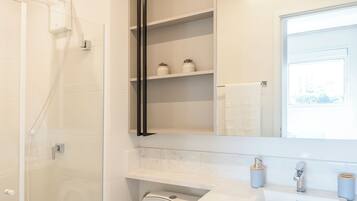 A modern bathroom with a glass shower enclosure, a white toilet, and a vanity with a mirror and shelves.