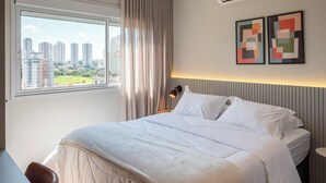 A modern bedroom with a large bed, a desk, a window with curtains, an air conditioning unit, and abstract wall art. - Charming Studio in Cambuí (Campinas)