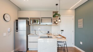 A modern kitchen with a stainless steel refrigerator, a built-in microwave, and a central island with bar stools. - Charming Studio in Cambuí (Campinas)
