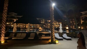 Een nachtzicht van het zwembadgedeelte van een resort, met ligbedden en palmbomen.