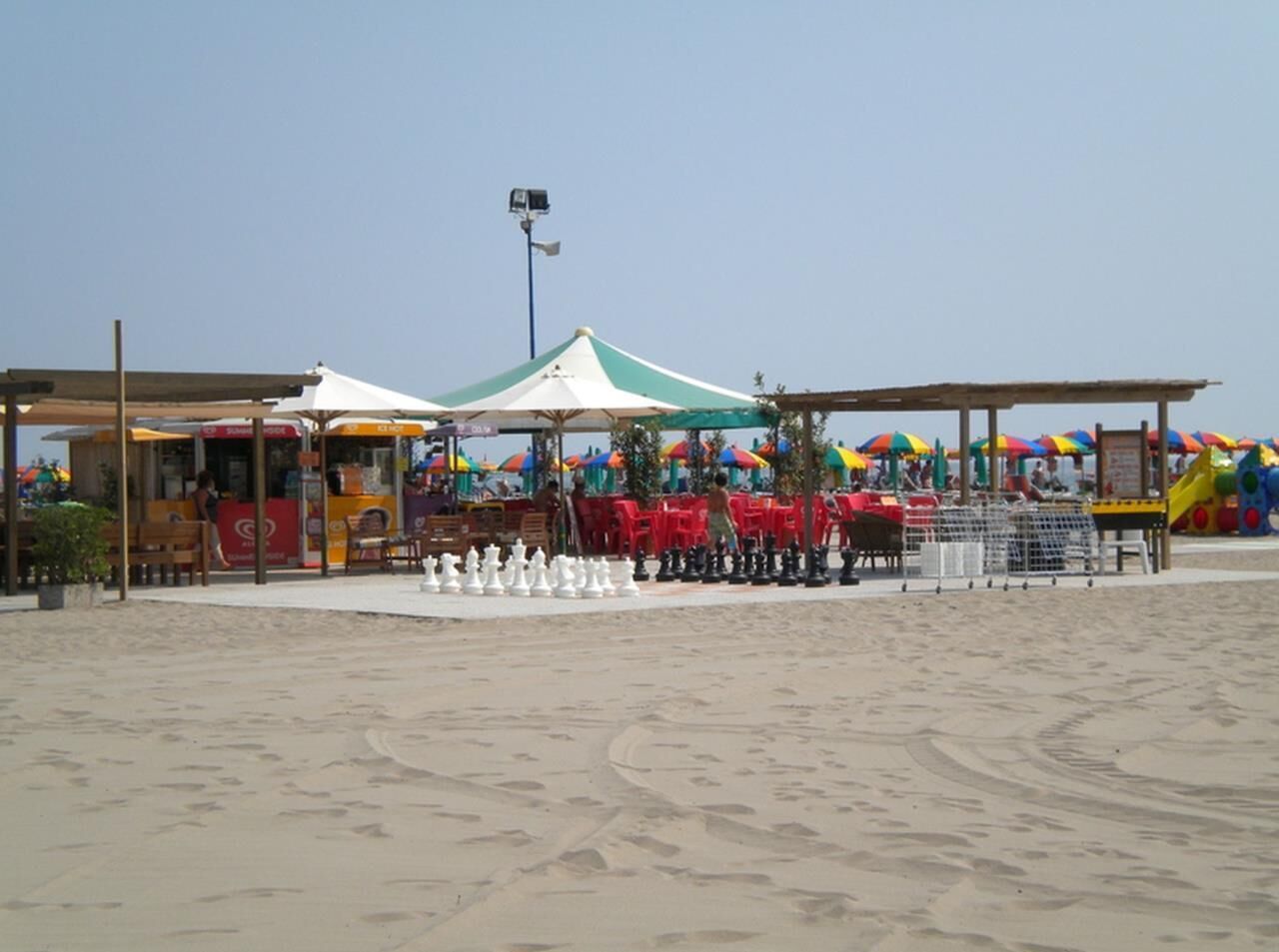 A beachside area with a food stall, umbrellas, and beach chairs.