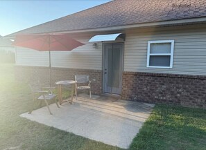 A residential building with a covered patio area featuring a red umbrella, two chairs, and a small table.
