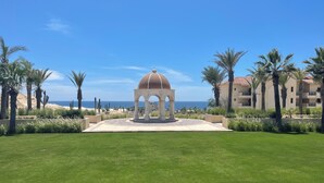 Un belvédère surmonté d’un dôme, entouré de pelouse bien entretenue et de palmiers, offrant une vue sur une plage et l’océan.