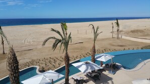 Un espace piscine doté de chaises longues et de parasols, offrant une vue sur une plage bordée de palmiers et un ciel d’un bleu limpide.