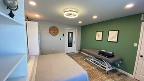 Une chambre à coucher avec un lit, une horloge, une petite table sur laquelle se trouvent divers objets, et un mur vert.