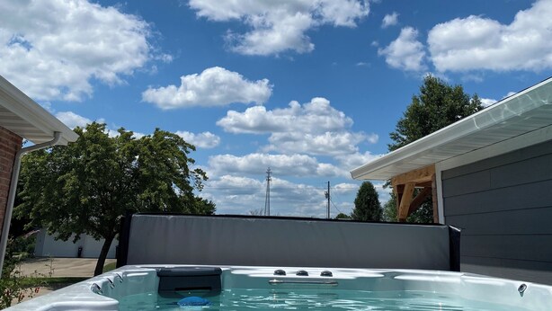 Un bain à remous dans un jardin, avec un ciel bleu dégagé et quelques nuages.