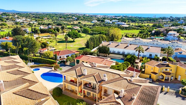 Una zona residenziale costiera con case a tetto in terracotta, una piscina e vista sul mare.