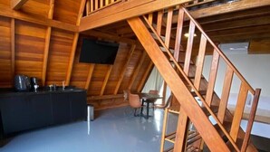 A loft-style room with a wooden staircase, a sofa, a coffee table, and a TV mounted on the wall. - LIMMAT CHALÉS (Presidente Juscelino)