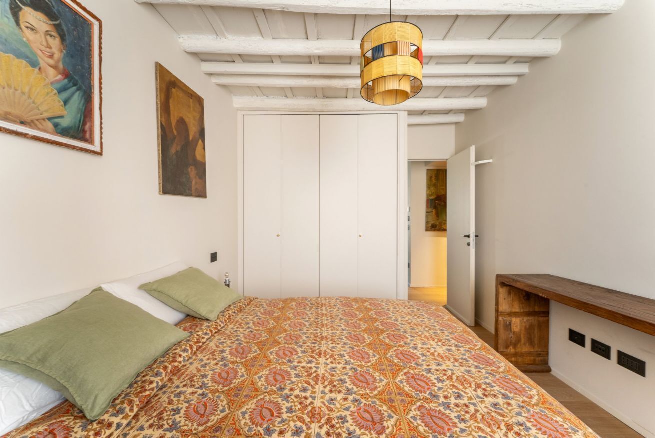 Ein Schlafzimmer mit einem gemusterten Bettbezug, einer Hängelampe, einem Kleiderschrank und einer Bank.