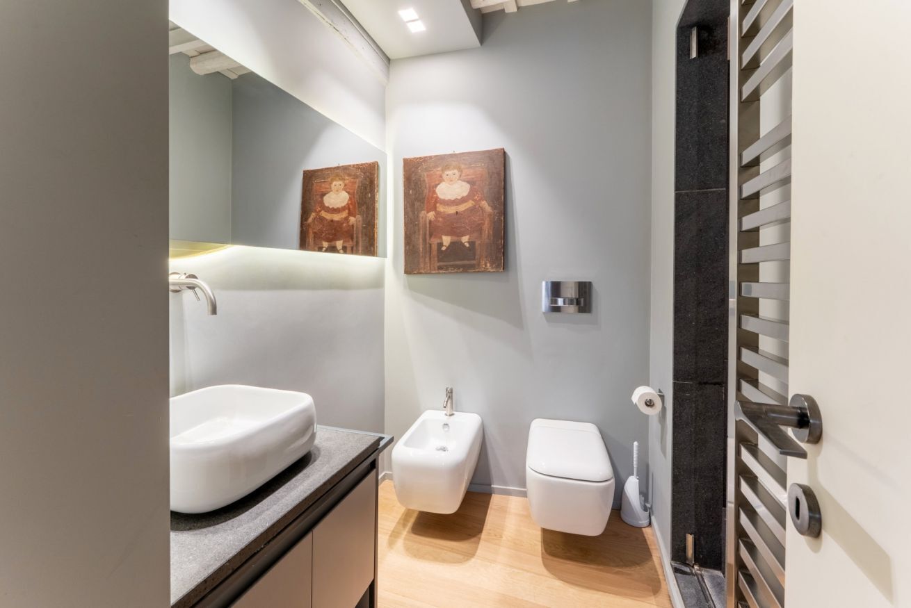A modern bathroom with a sink, bidet, toilet, and artwork on the wall.