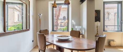 Een eetruimte met een houten tafel en stoelen, grote ramen met uitzicht op gebouwen en hangende hanglampen.