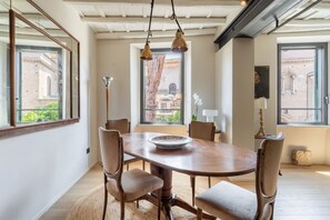 A dining area with a wooden table and chairs, large windows with views of buildings, and hanging pendant lights. - Zenaria Trastevere, Zen Design in Heart of Rome (Rome)