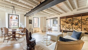 Un vaste salon doté d’un haut plafond, un coin repas avec une table ronde et des chaises, et un paravent de style asiatique traditionnel.