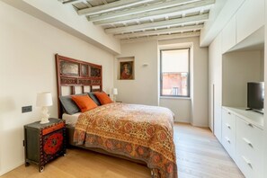 Un dormitorio con cama, mesita de noche, televisión y ventana.