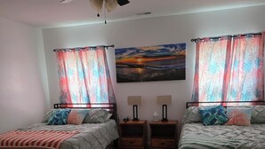 Quarto com duas camas, ventoinha no teto, um quadro e cortinas.