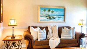 Uma sala de estar acolhedora com um sofá marrom, duas mesas laterais com luminárias e uma pintura de uma praia emoldurada na parede.