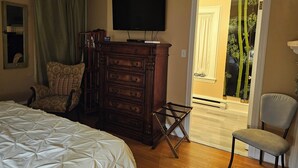 A bedroom with a bed, a dresser, a chair, a television, and a door leading to a balcony. - TTR - Kensington (Pembroke)