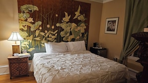 A neatly made bed with a white duvet, a wooden headboard with floral artwork, a bedside lamp, and a small table with a clock and books. - TTR - Kensington (Pembroke)