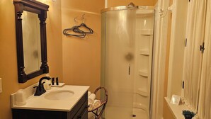 A bathroom with a vanity, mirror, towel rack, shower, and a small potted plant. - TTR - Kensington (Pembroke)