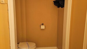 A small, narrow bathroom with a toilet, a roll of toilet paper on the wall, and a shelf with a decorative item. - TTR - Kensington (Pembroke)