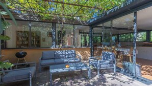 Een buitenpatio met glazen omheining, een bank, een tafel en een barbecue.