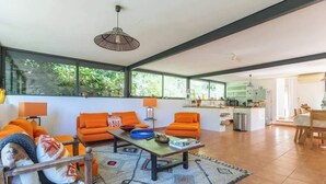 Een ruime woonkamer met oranje banken, een houten bijzettafeltje en een groot raam met uitzicht op groen.