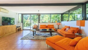 Een moderne woonkamer met oranje meubels, grote ramen en een televisie.