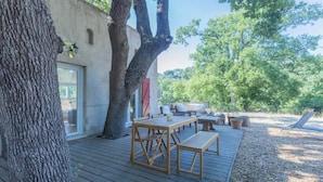 A wooden deck with outdoor furniture, a tree, and a building with a glass door.