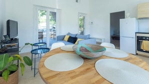 A modern living room with a sofa, coffee table, and a TV. There are two doors leading to a balcony.