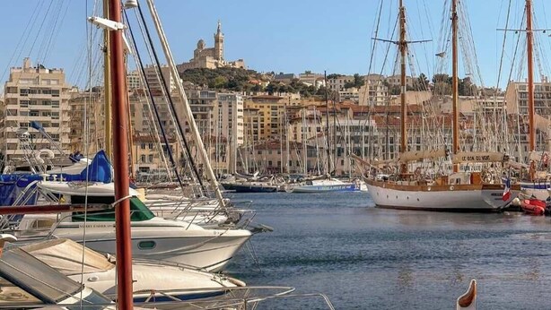 A marina with several sailboats docked, a prominent building with a tower in the background, and a clear sky. - Nid du 5ème - Proche Bd Baille - Métro et commerce (Marseille)