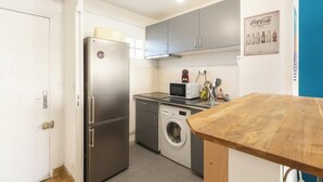 A compact kitchen with a refrigerator, microwave, washing machine, and wooden table. - Nid du 5ème - Proche Bd Baille - Métro et commerce (Marseille)