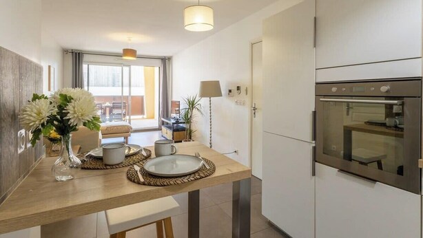 A modern kitchen with a wooden countertop, a built-in oven, and a dining area with a table set for two. - La Terrasse de Duranne - Accès rapide TGV Aéroport (Aix-en-Provence)