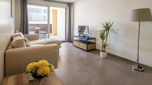 A modern living room with a sofa, a coffee table with flowers, a TV stand, a potted plant, and a floor lamp. - La Terrasse de Duranne - Accès rapide TGV Aéroport (Aix-en-Provence)