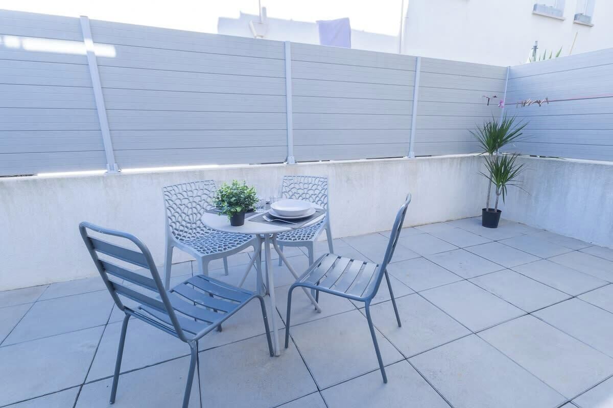 A patio with a table and two chairs, a small potted plant, and a metal fence.