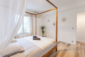 Un lit à baldaquin, une plante en pot et des œuvres d’art décoratives sur les murs, dans une chambre d’hôtel.