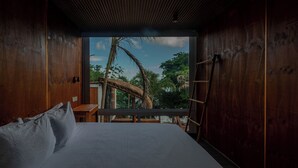 A room with a bed, wooden walls, a window with a view of palm trees and a thatched-roof structure. - Tregua (Bacalar)