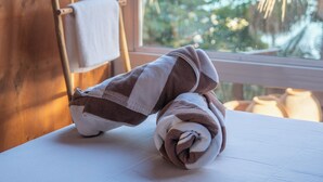 A wooden ladder leaning against a wall with white towels hanging on it. A rolled towel is on a table in front of a window with a view of palm trees. - Tregua (Bacalar)