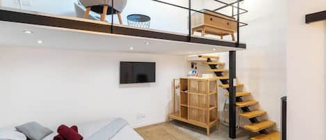 Ein modernes Schlafzimmer im Loft-Stil mit Schlafgalerie, integriertem Fernseher, Holztreppe und einer kleinen Sitzecke mit Stuhl und Tisch.