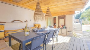 An outdoor dining area with a wooden deck, a table set for four, and hanging wicker lamps. - Studio Terra'ciel - Proche calanques - Piscine (La Ciotat)