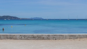 A beach with a concrete barrier, calm water, and sailboats. - Studio Terra'ciel - Proche calanques - Piscine (La Ciotat)