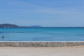 Une plage avec une barrière en béton, une eau calme et des voiliers.