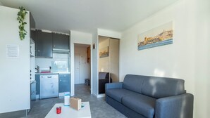 Um apartamento moderno com um sofá cinzento, uma mesa de centro branca e uma área de cozinha visível por uma porta aberta.
