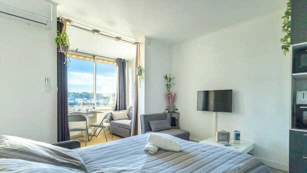 Quarto de hotel com duas camas, uma escrivaninha, uma cadeira, uma televisão e varanda com vista.