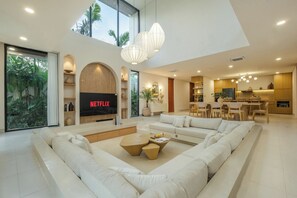 Ein geräumiges Wohnzimmer mit einer großen Eckcouch, einem Couchtisch und einem Flachbildfernseher, der 'NETFLIX' zeigt.