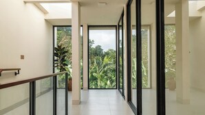 Un pasillo interior moderno con puertas de vidrio que dan a un balcón con vistas a vegetación exuberante.