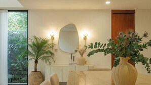 A modern dining area with a large table, chairs, a vase of flowers, a potted plant, and a mirror with wall sconces. - Quiet Luxury Villa Uluwatu. Private Pool, Workspace, Airport Pick Up & Butler (Bali)