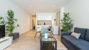 Una sala de estar moderna con un sofá, un televisor, una mesa de centro de vidrio y dos plantas en macetas.