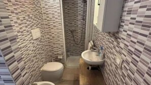 Une salle de bain comprenant des toilettes, un bidet et un lavabo, avec des murs carrelés et un espace douche.